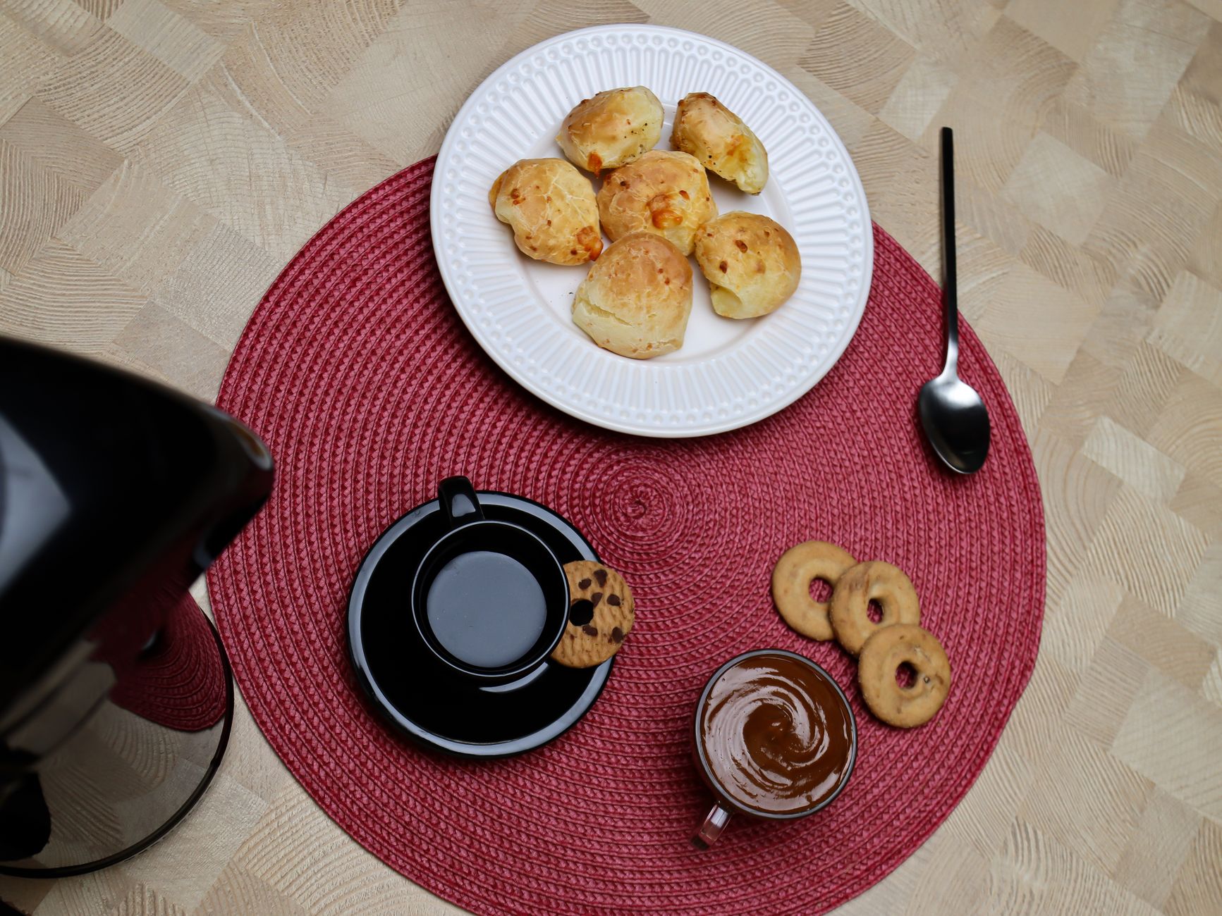 Overhead view of a breakfast setup with coffee, pastries, and cookies on a red mat.