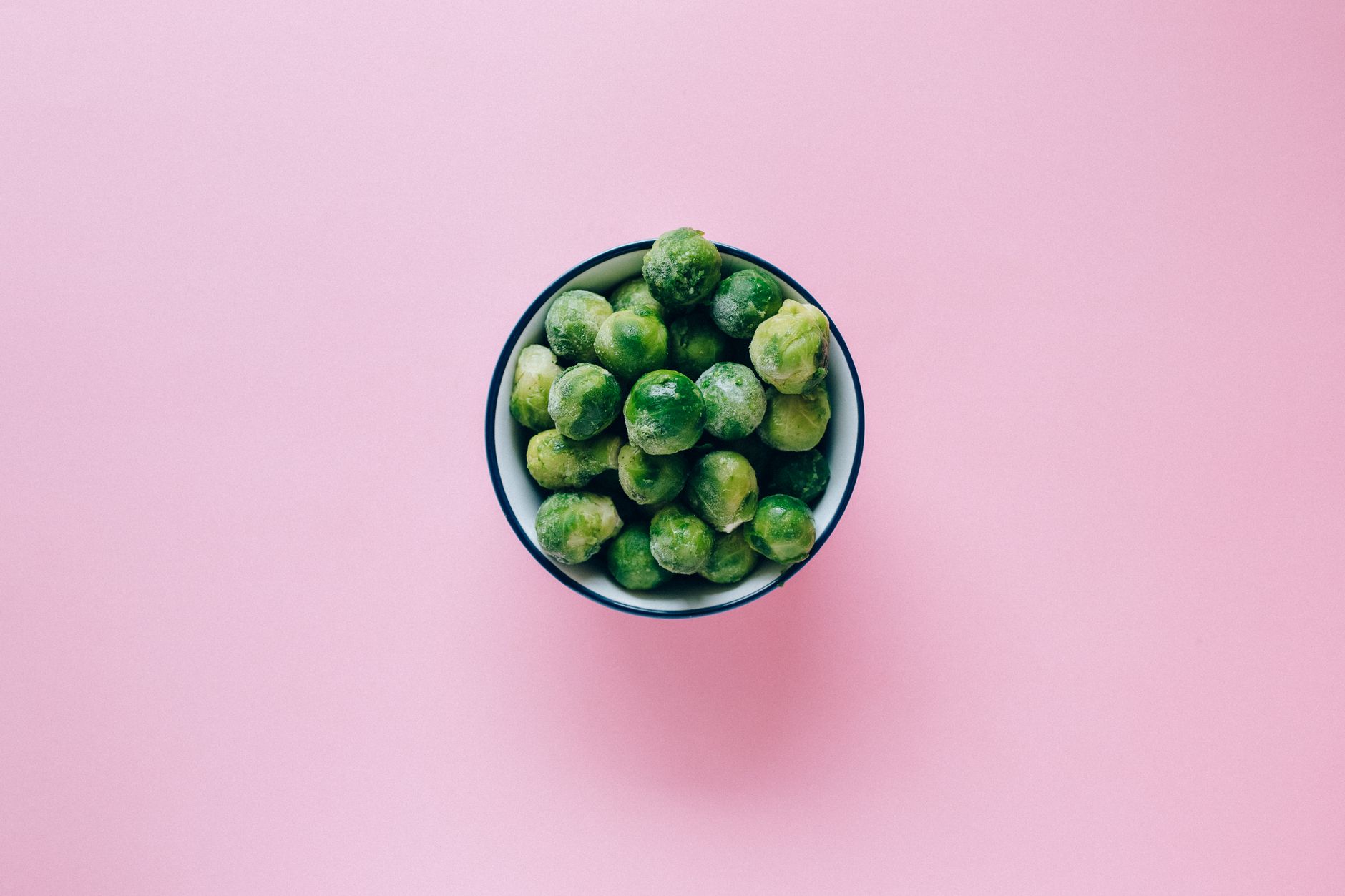 Overhead shot of frozen green peas in a bowl against a vibrant pink background.