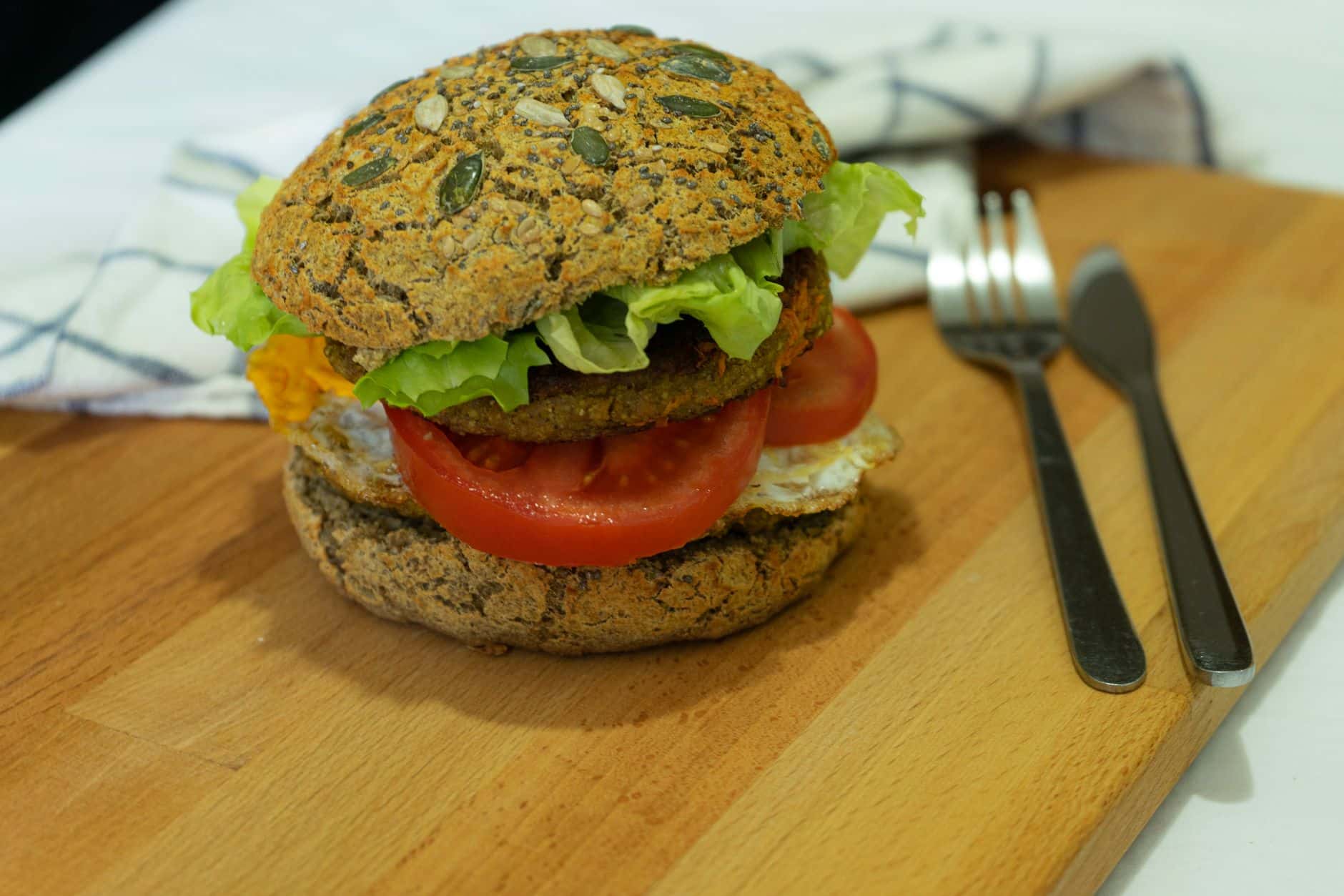 Close-up of a nutritious vegan burger with fresh tomato, lettuce, and seeds on a wooden board.