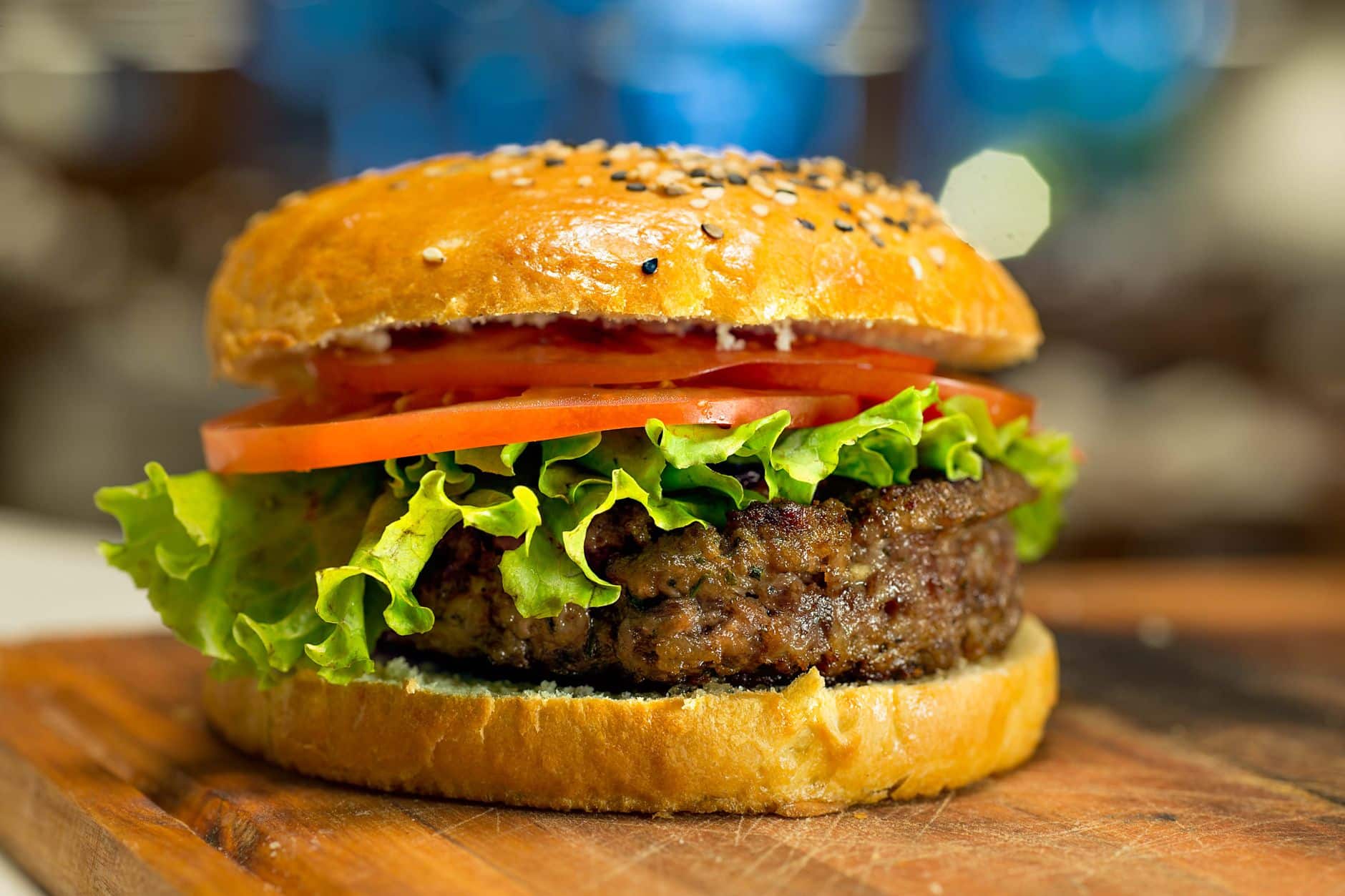Mouthwatering close-up of a beef burger with lettuce, tomato, and sesame seed bun.