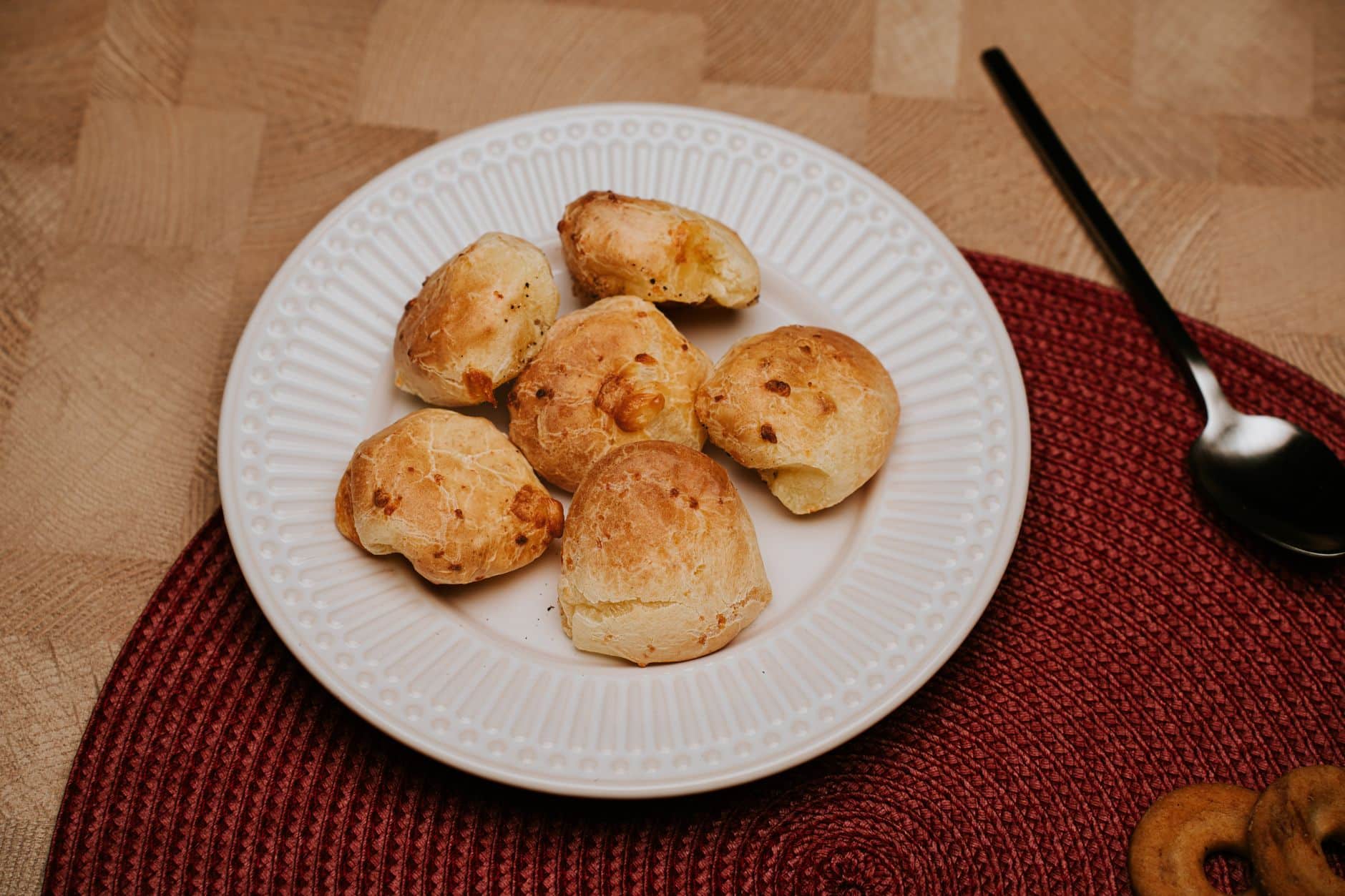 Plate of traditional Brazilian cheese bread rolls on a red mat with a spoon.
