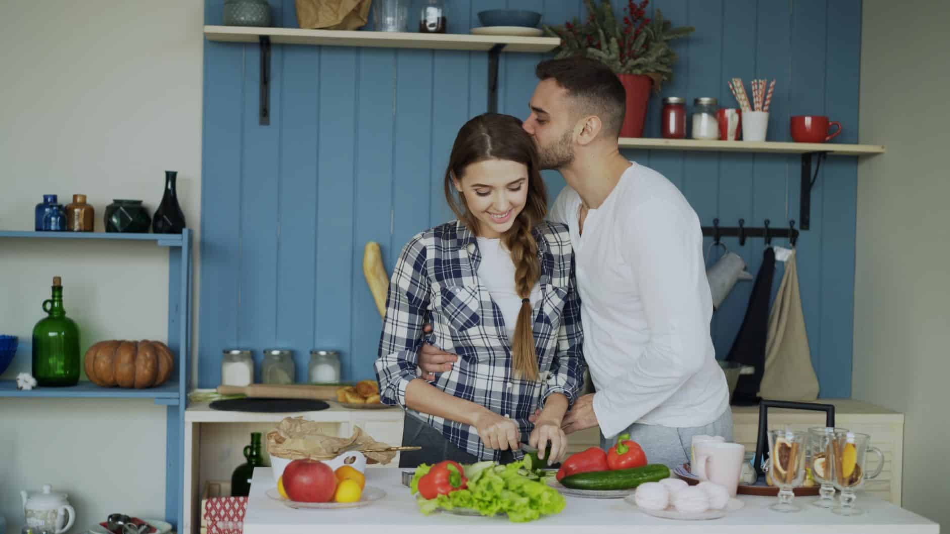 A loving couple enjoys cooking together in a cozy, well-decorated kitchen at home.