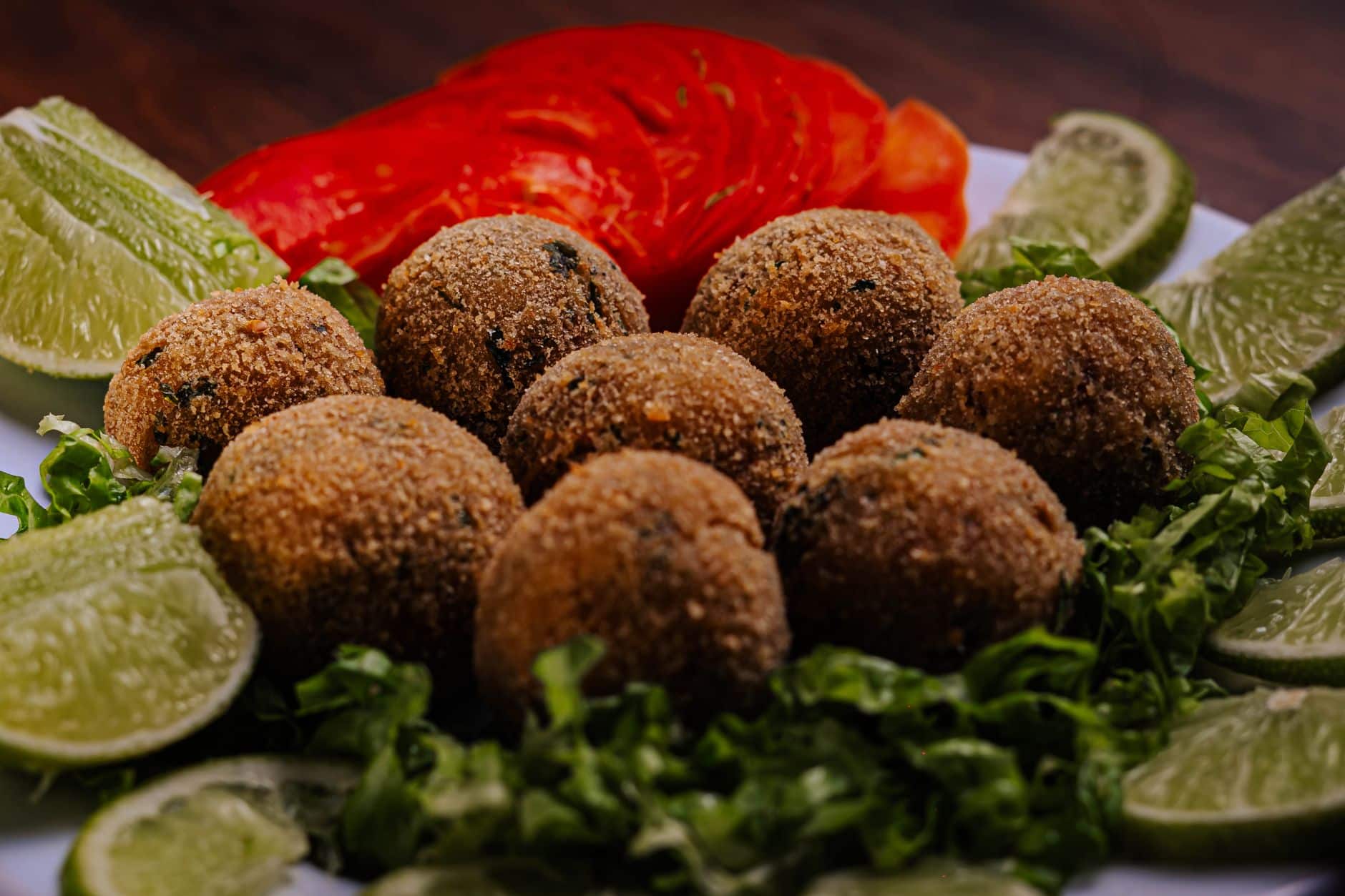Crispy falafel balls served with fresh lime and tomato slices on a bed of lettuce.