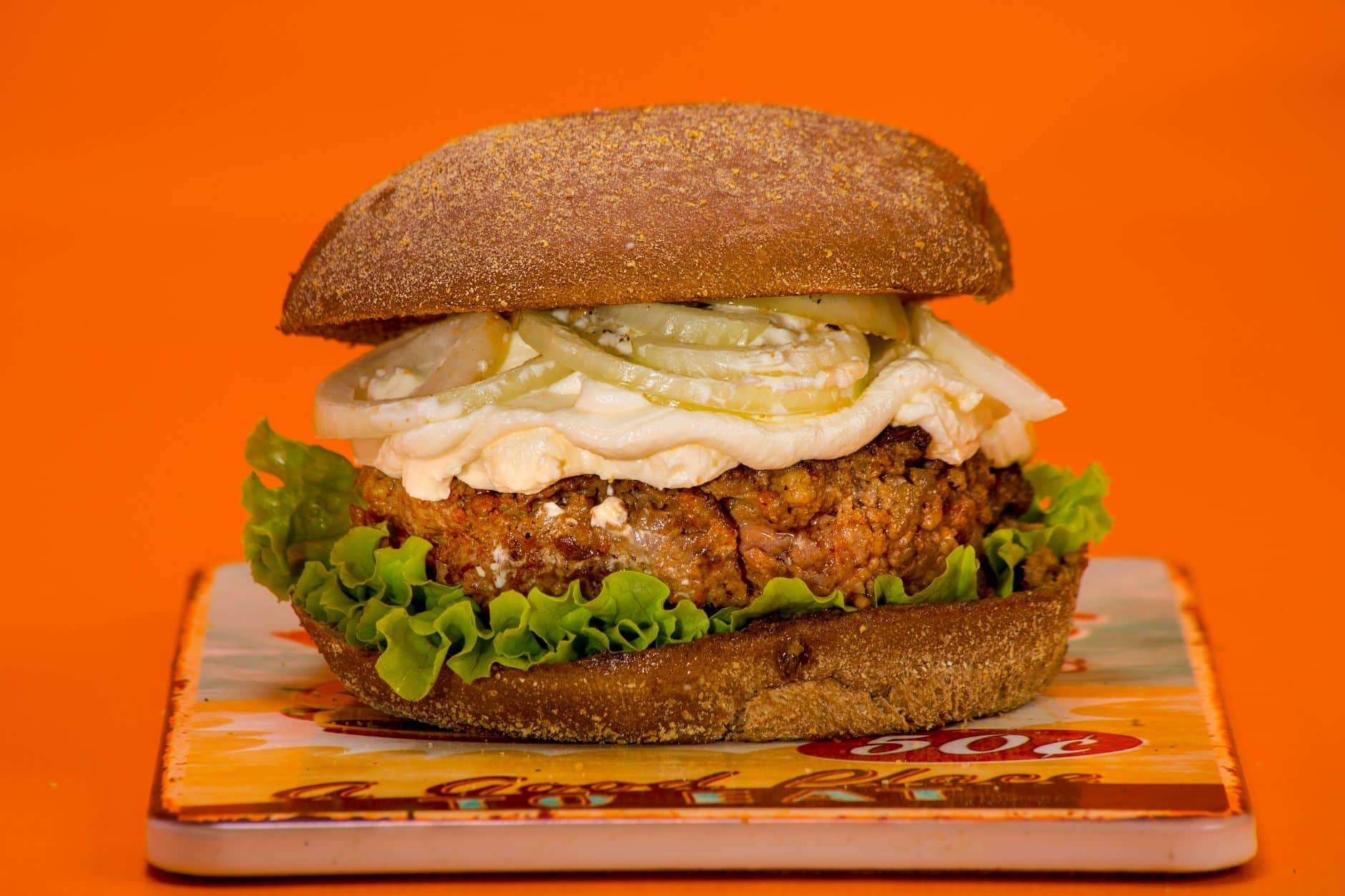 Delicious hamburger with fresh lettuce, pickles, and a thick patty on a vibrant orange backdrop.
