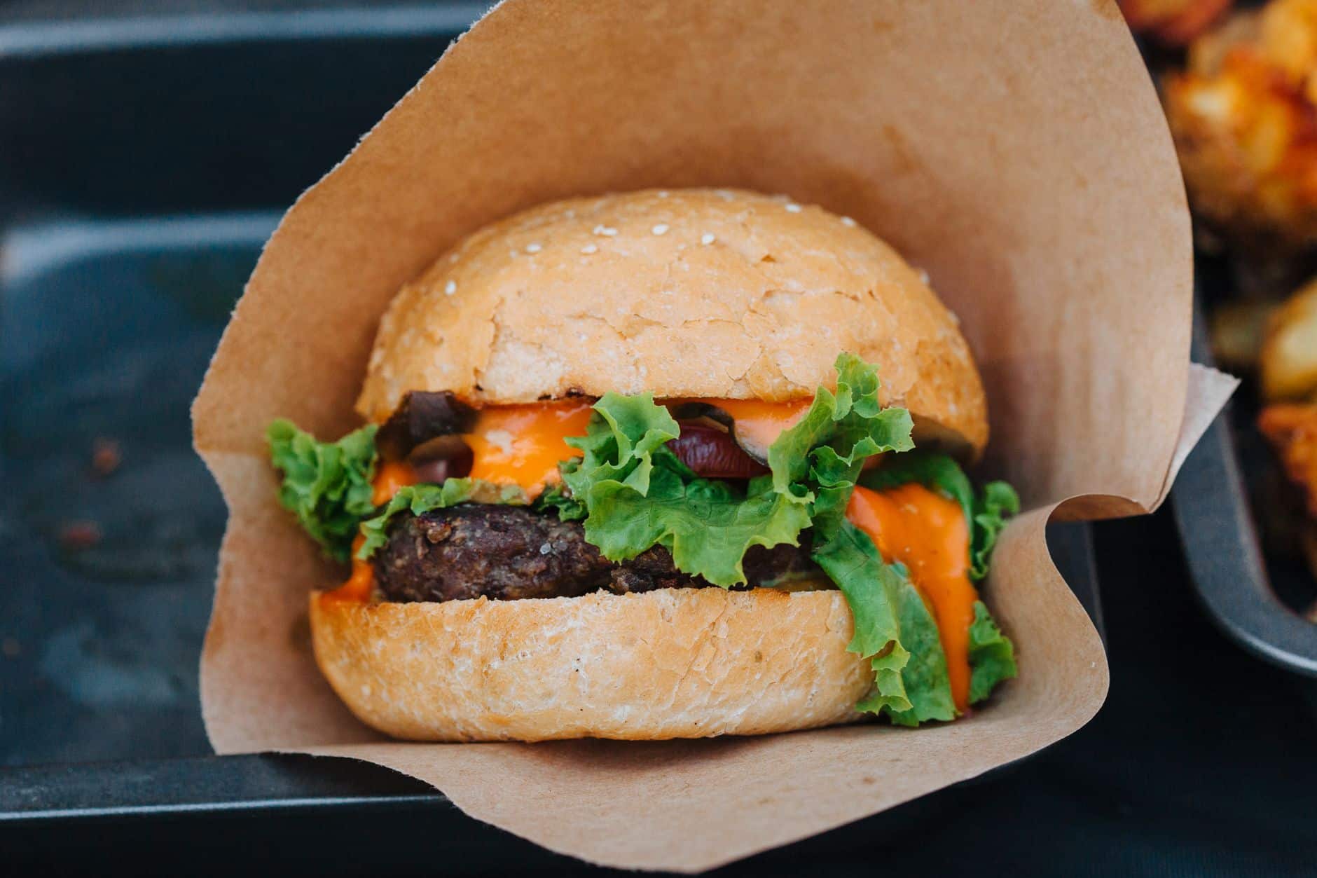 Close-up of a delicious cheeseburger with fresh lettuce and creamy sauce wrapped in paper.