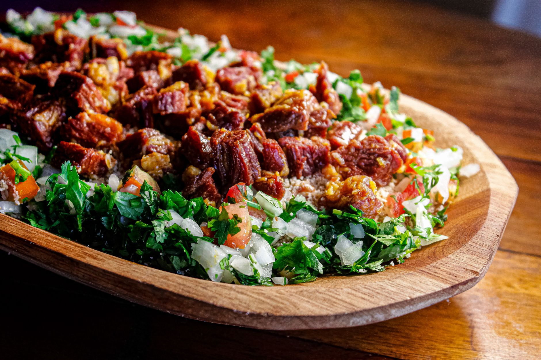 A vibrant serving of Brazilian carne de sol with fresh herbs and vegetables on a wooden platter.