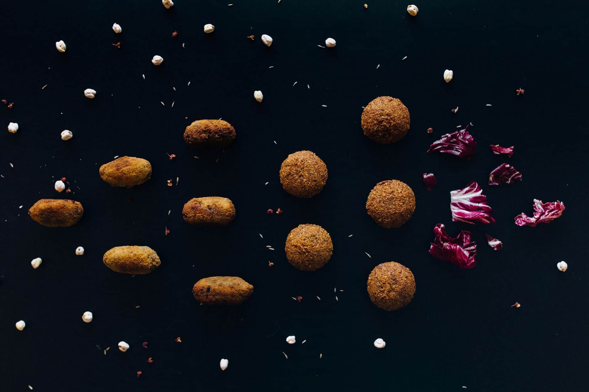 A minimalist flat lay of falafel with chickpeas and red cabbage on a black surface.