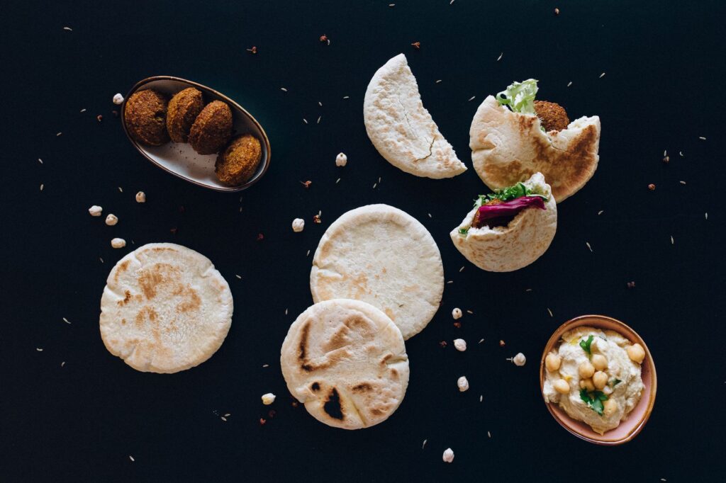Flatlay of pita bread, hummus, and falafel on a dark background.