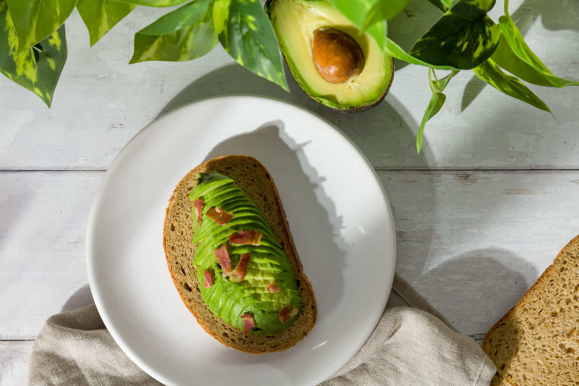 Healthy avocado toast with bacon on a white plate in natural light.