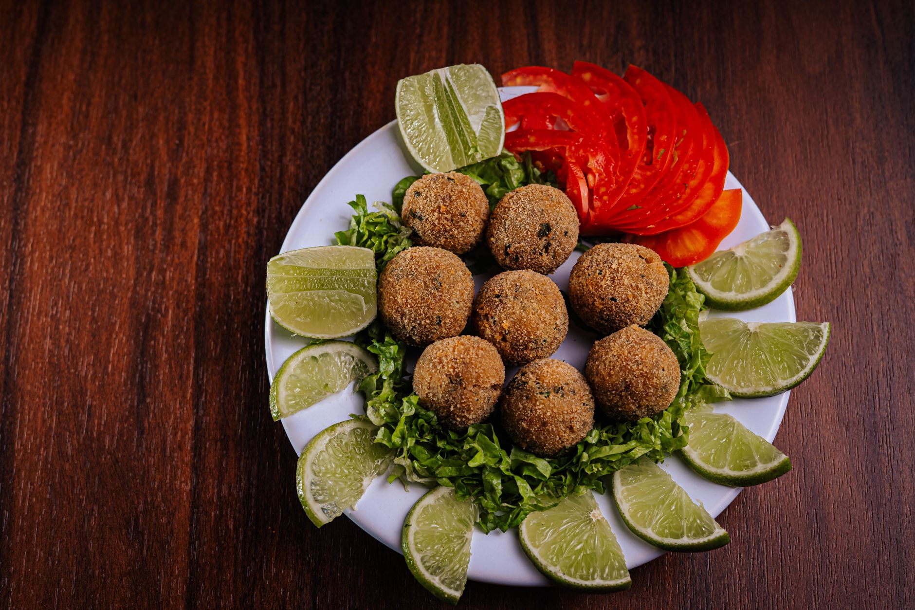 Crispy fried balls served with fresh lime and sliced tomato on a bed of lettuce.