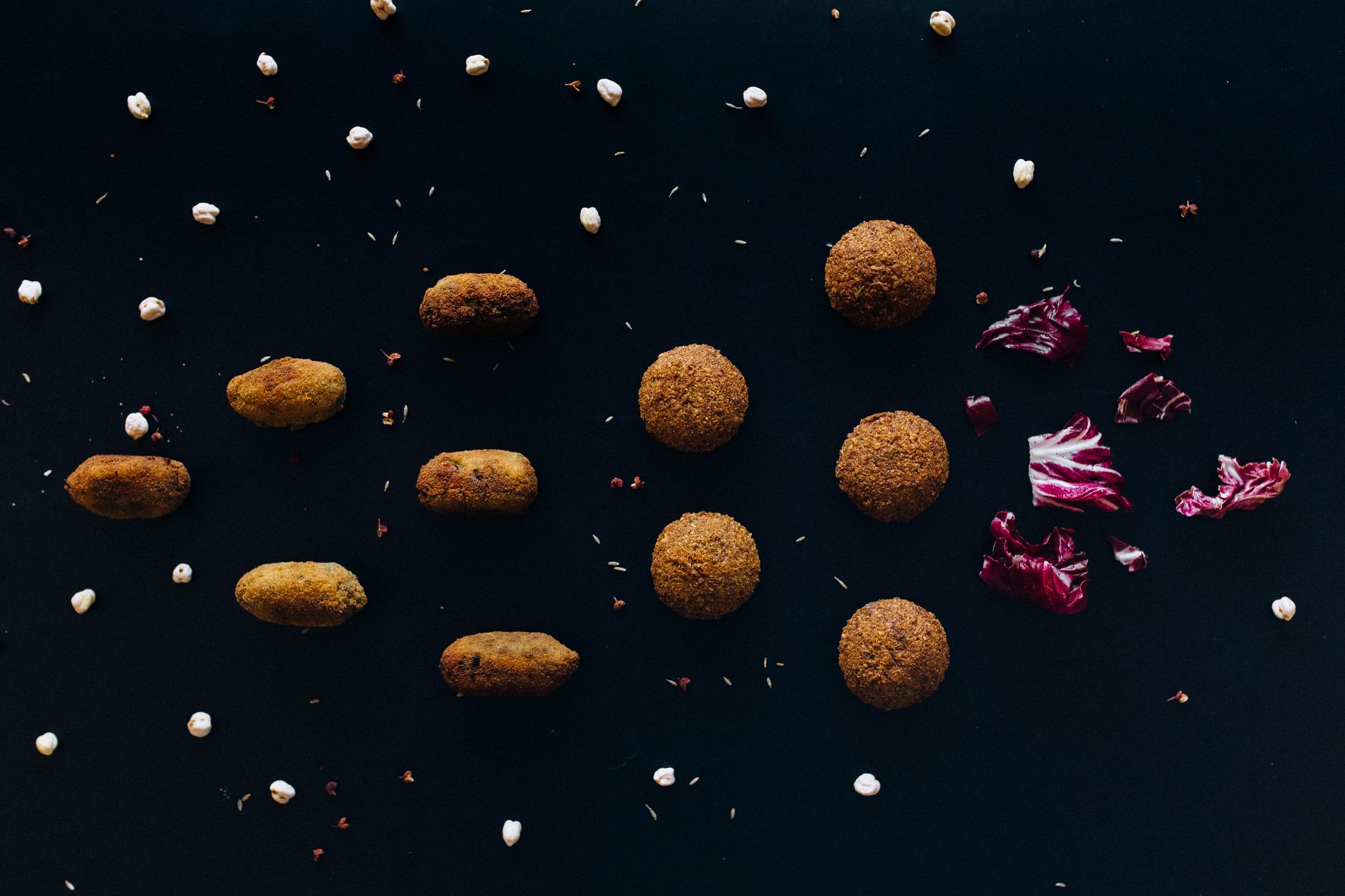 A minimalist flat lay of falafel with chickpeas and red cabbage on a black surface.