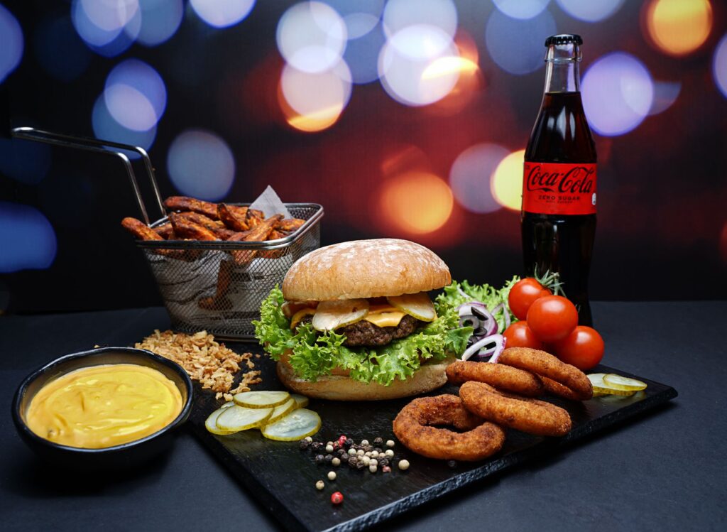 A gourmet burger with sides, sauce, and cola on a vibrant bokeh backdrop.