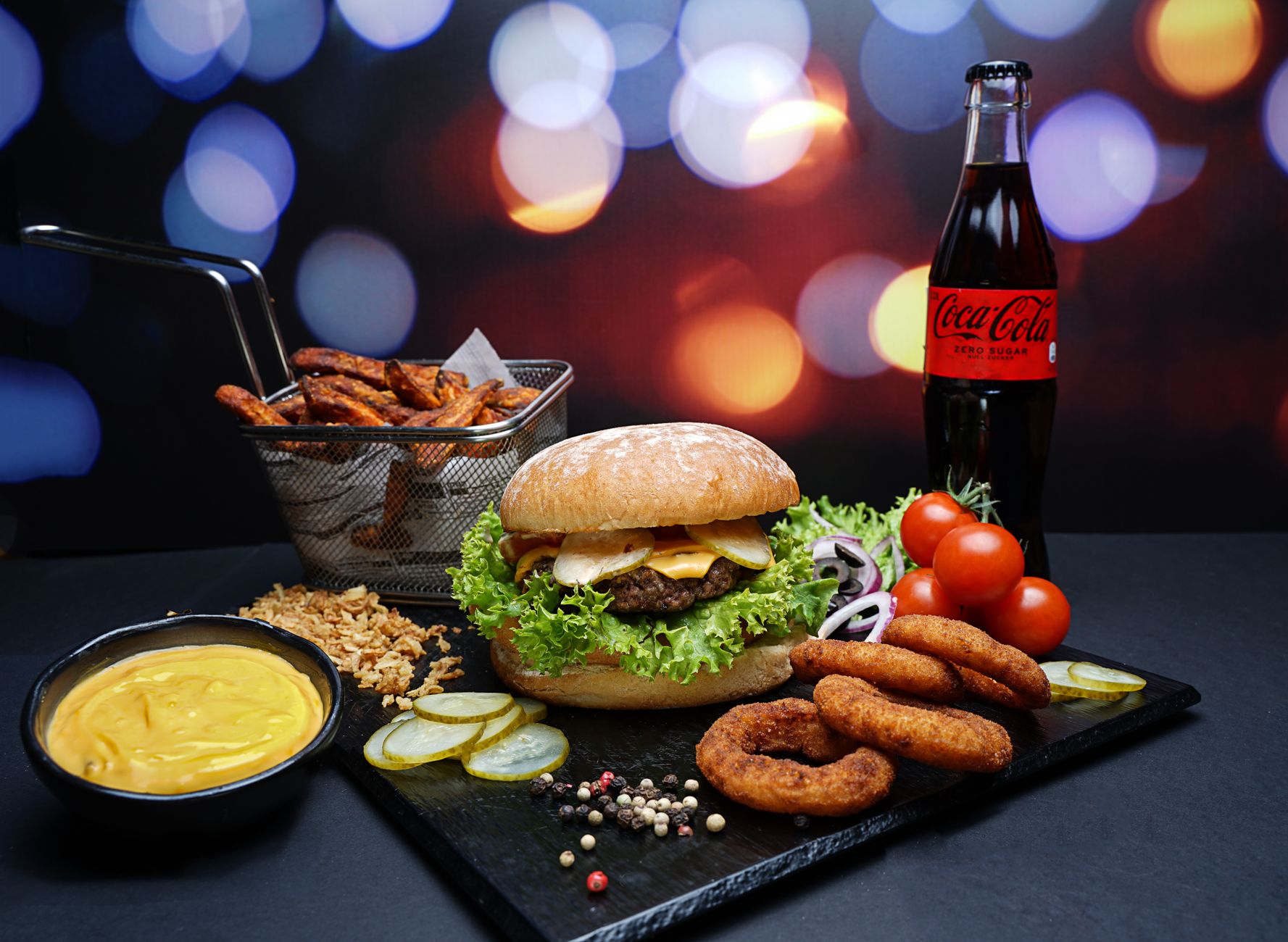 A gourmet burger with sides, sauce, and cola on a vibrant bokeh backdrop.