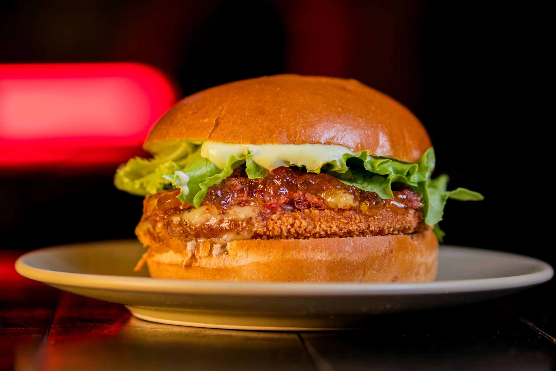 A close-up of a crispy chicken burger with lettuce and mayonnaise on a plate.