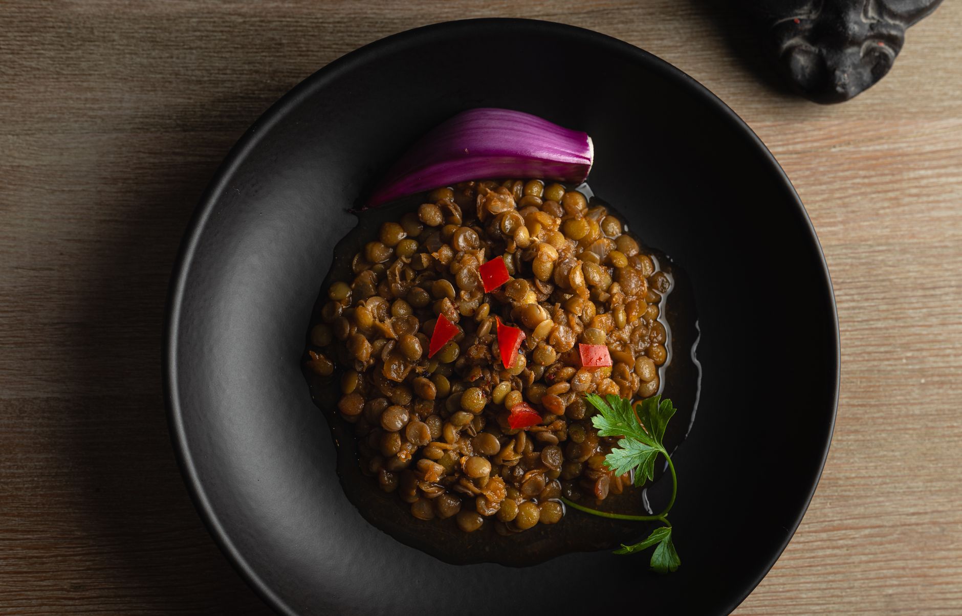 Top view of a savory lentil dish garnished with onion and parsley in a black bowl.