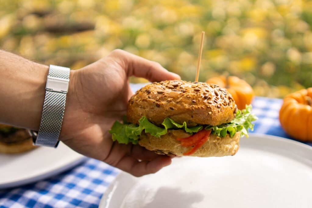 Close-up of a veggie burger with lettuce and tomato being held at a picnic.