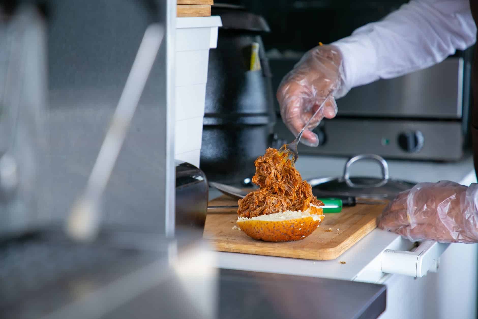 Side view of crop anonymous male chef in gloves preparing tasty hamburger with roast meat in kitchen