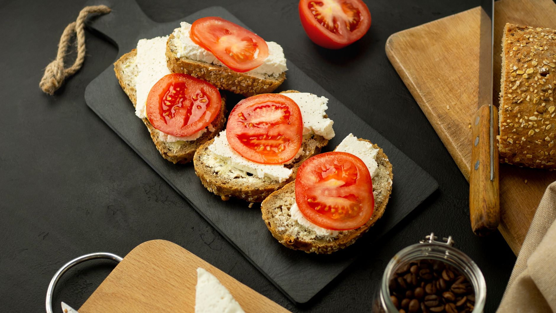 Sliced wholegrain bread with cream cheese and fresh tomatoes on a black board, perfect snack idea.