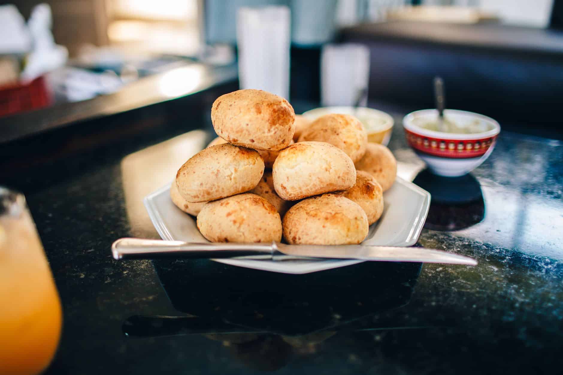 From above of tasty crispy baked buns with golden surface on plate with knife near bowls with butter for breakfast on marble table at home