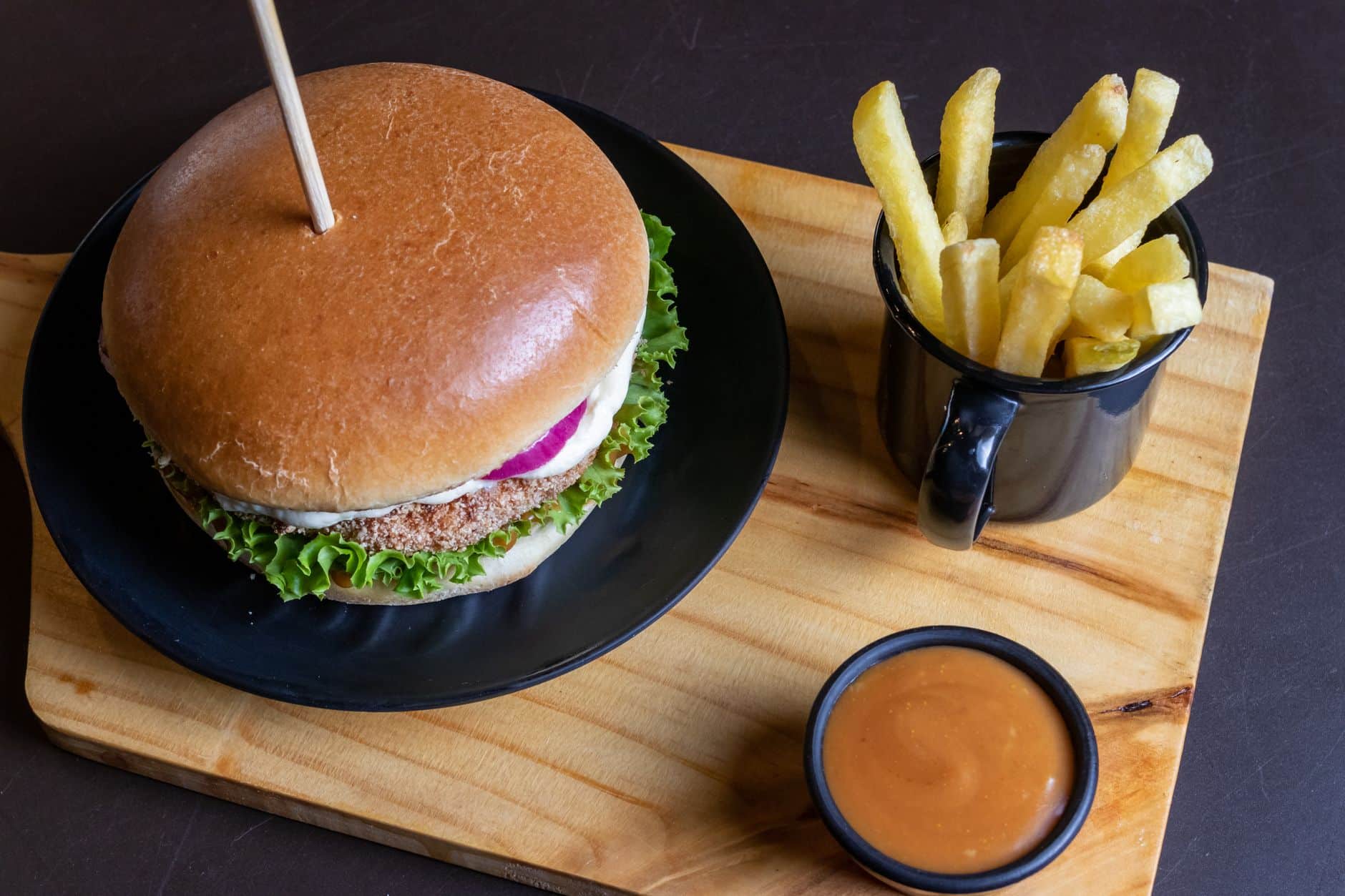 Top view of a tasty burger with fries and sauce on a wooden board.